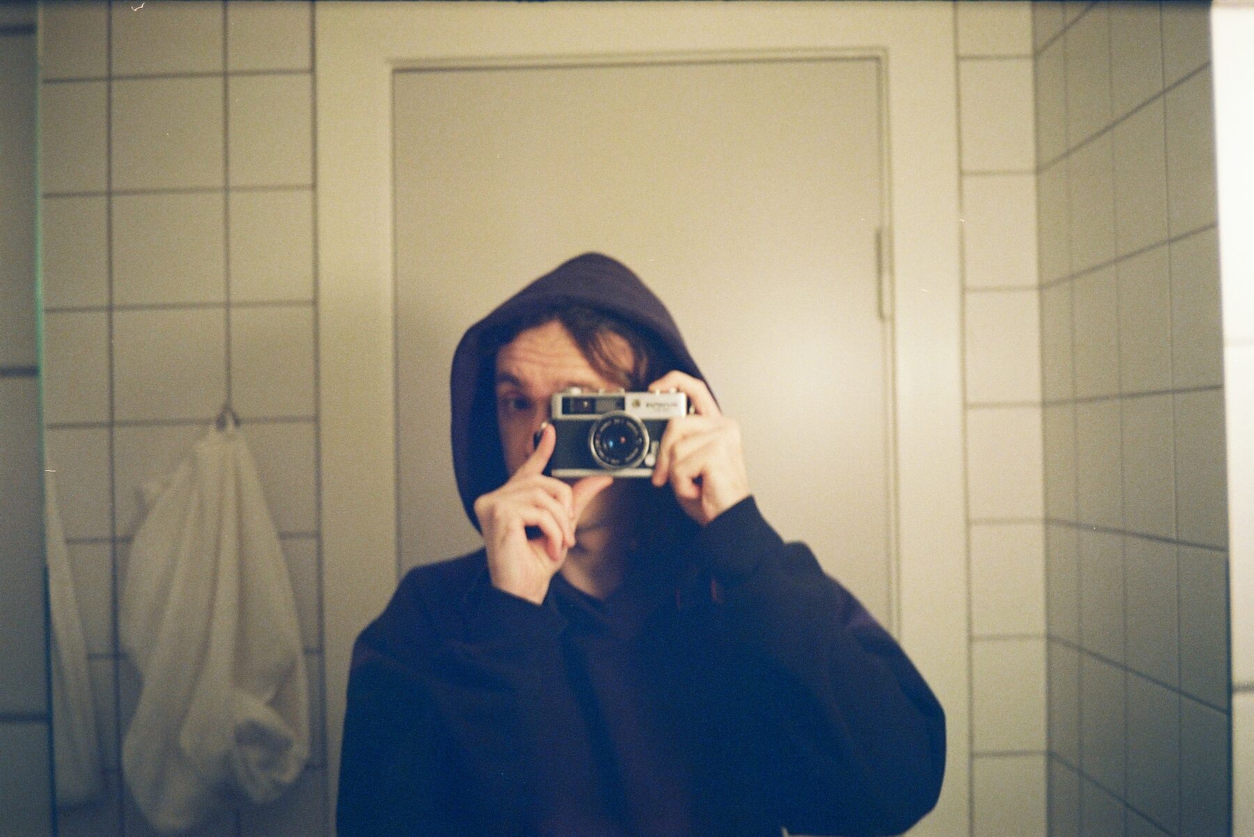 Katherine Bellingham photographing her reflection in a tiled bathroom mirror
